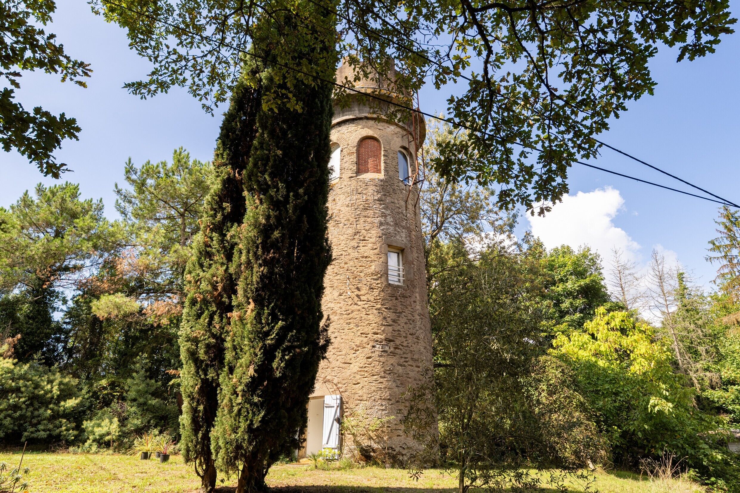 A stone tower with arched windows, surrounded by trees and greenery.