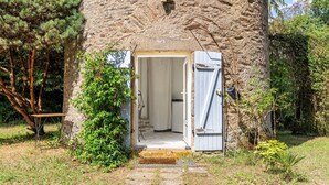 A rustic stone building with a wooden door, a small table, and a chair outside. - Holiday Home 'Le Moulin De Pen Hoêt' with Shared Garden (Vertou)