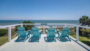 Une terrasse avec quatre chaises Adirondack turquoise, disposées face à une plage.