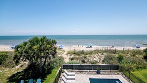 A beach view with a pool area, palm trees, and beach umbrellas.