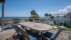 A wooden deck with a pool table, lounge chairs, and a view of the ocean.