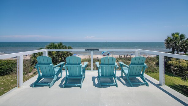 A deck with four turquoise Adirondack chairs facing the ocean.