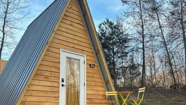 Une petite cabane triangulaire en bois, avec une porte blanche et une plaque portant le numéro « 23 ».
