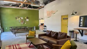 Un salon meublé avec un mur vert, un canapé en cuir marron, une table basse en bois et des coussins jaunes.