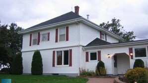 A two-story house with a gabled roof, a chimney, and a front porch. - Linden Homestead: Modern Queen Bed B&B suite in Century Farm House (Stanley Bridge)