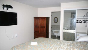 A bedroom with a bed, a wooden wardrobe, a television mounted on the wall, and a bathroom visible through an open door. - Linden Homestead: Modern Queen Bed B&B suite in Century Farm House (Stanley Bridge)