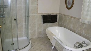 A bathroom with a glass shower enclosure, a white bathtub, and a tiled floor. - Linden Homestead: Modern Queen Bed B&B suite in Century Farm House (Stanley Bridge)
