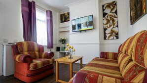 A living room with a sofa, armchair, and a small wooden table. - 12 Cornwallis Lodge Family Room 2 (Stoke-on-Trent)