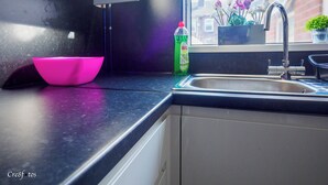 A kitchen with a black countertop, a pink bowl, a green bottle, and a window with flowers. - 12 Cornwallis Lodge Family Room 2 (Stoke-on-Trent)