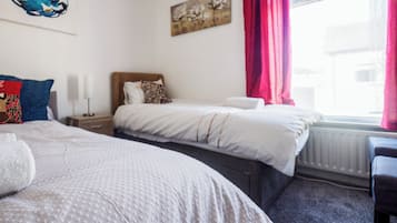 Een hotelkamer met twee bedden, een nachtkastje, een lamp, een schilderij en een raam met gordijnen.
