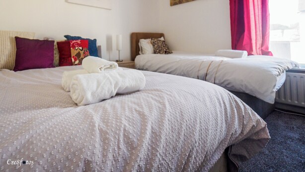 A hotel room with two beds, a painting on the wall, and a window with curtains. - 12 Cornwallis Lodge Family Room 2 (Stoke-on-Trent)