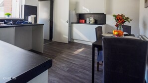 A compact kitchen with white cabinets, a black countertop, and a dining area with a table set for two. - 12 Cornwallis Lodge Family Room 2 (Stoke-on-Trent)