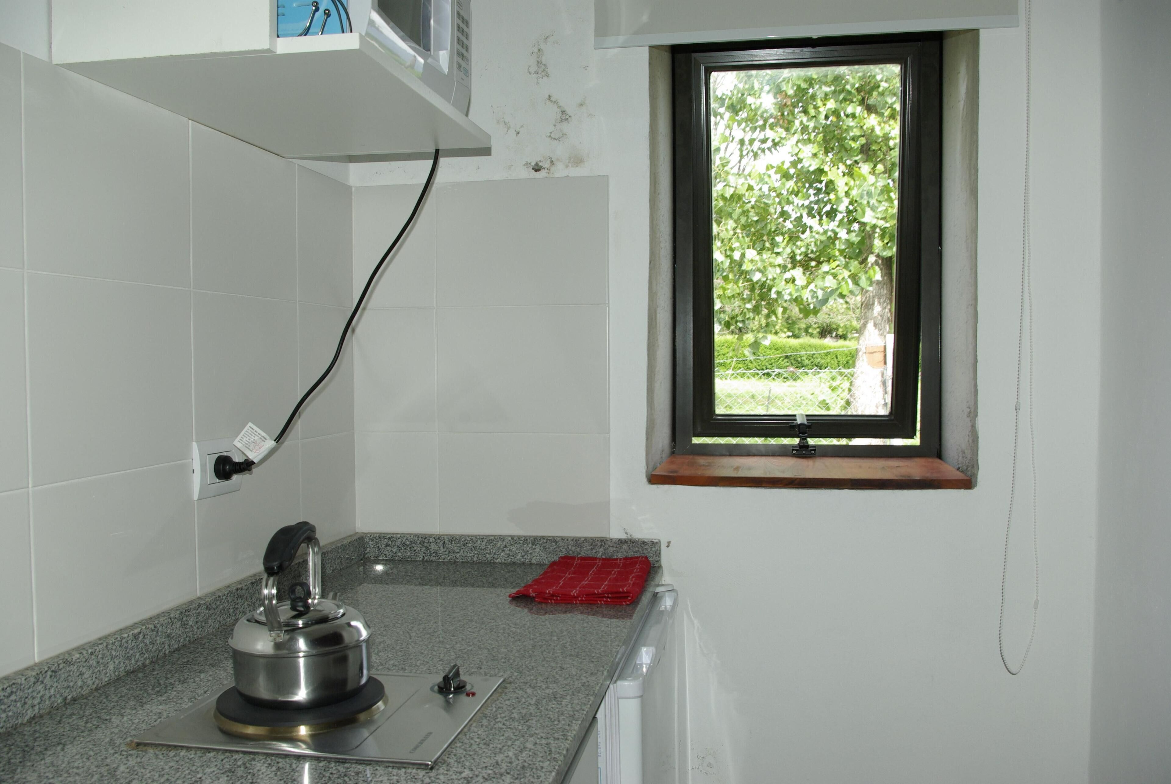 A kitchen with a kettle, a window, and a red towel on the counter.