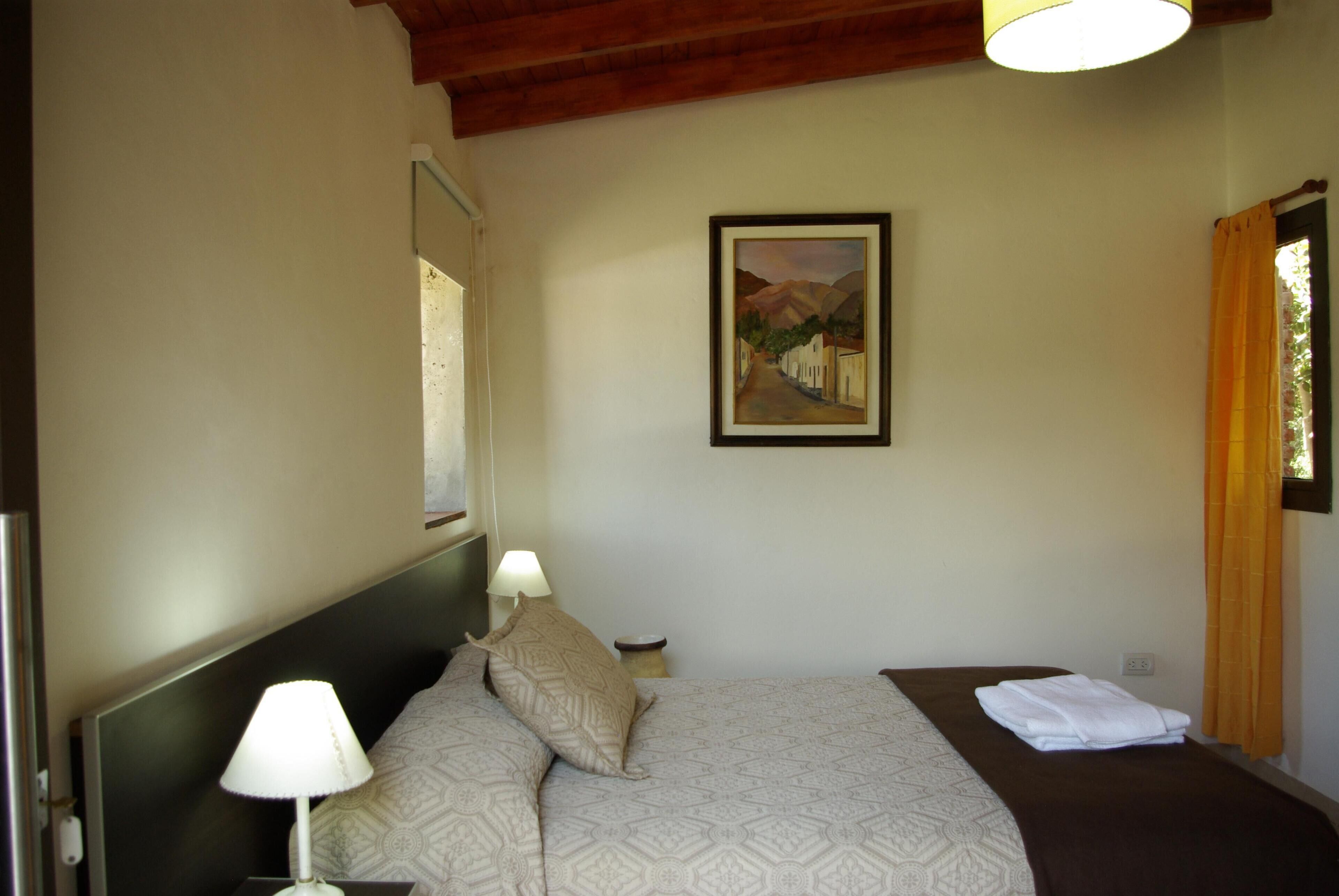 A hotel room with a bed, two bedside lamps, a painting on the wall, and a window with curtains.