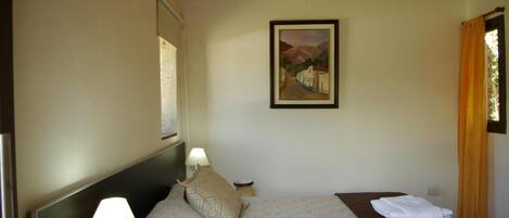 A hotel room with a bed, two bedside lamps, a painting on the wall, and a window with curtains.
