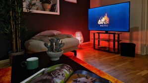Un saló amb un televisió de pantalla plana que mostra el logotip de 'Walt Disney PICTURE', un sofà, una planta de cactus, una làmpada i una taula de cafè amb una tassa i una revista.