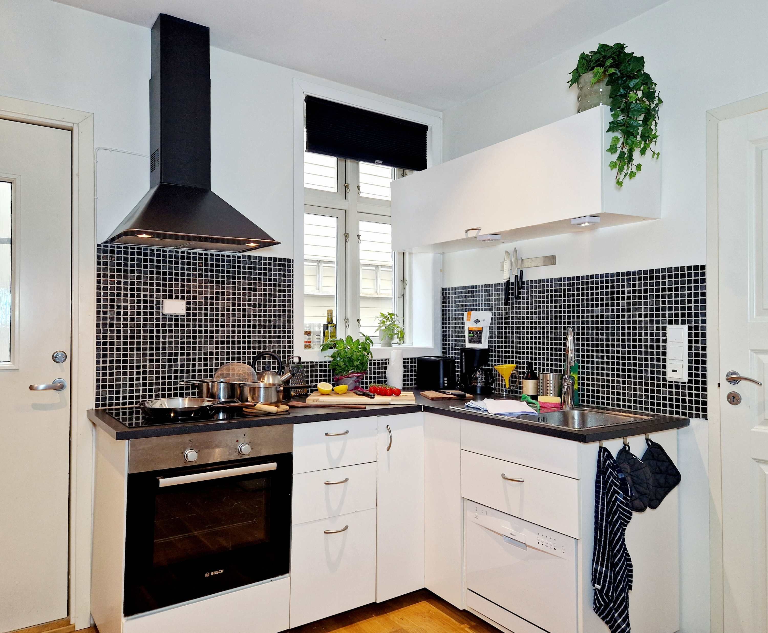 A modern kitchen with white cabinets, a black Bosch oven, a black range hood, and a black and white tiled backsplash.