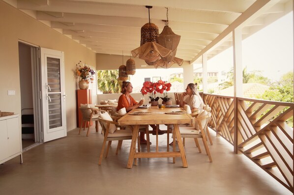 A dining area with a wooden table and chairs, hanging wicker lamps, and a view of greenery outside. - Yucca mini boutique hotel - Adults only (Jan Thiel)
