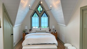 Een slaapkamer met een schuine kap, een groot bed, twee nachtkastjes met lampen, en een raam met uitzicht.