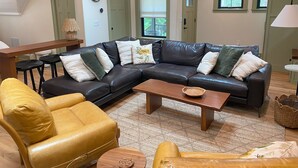 Een woonkamer met een hoekbank, een gele fauteuil, een houten salontafel en een geweven mand.