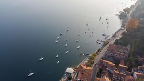 An aerial view of a coastal town with boats docked along the waterfront, buildings with traditional architecture, and a road leading into the town. - Apartment 'Nido Blu - Cosy Home' with Lake View, Wi-Fi and Air Conditioning (Belgirate)