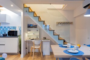 A modern kitchen with a microwave, a small dining table with blue placemats, and a staircase leading to another level.