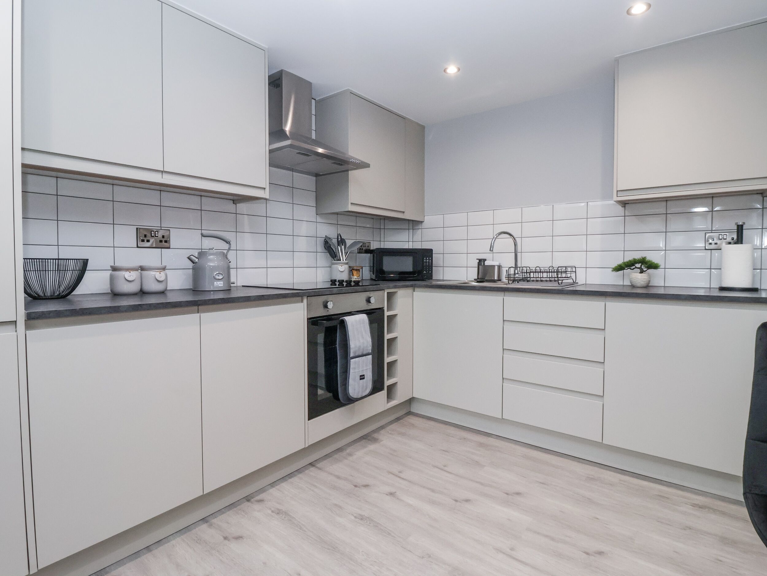 Una cocina moderna con armarios blancos, una campana extractora de acero inoxidable, un microondas y un lavamanos.