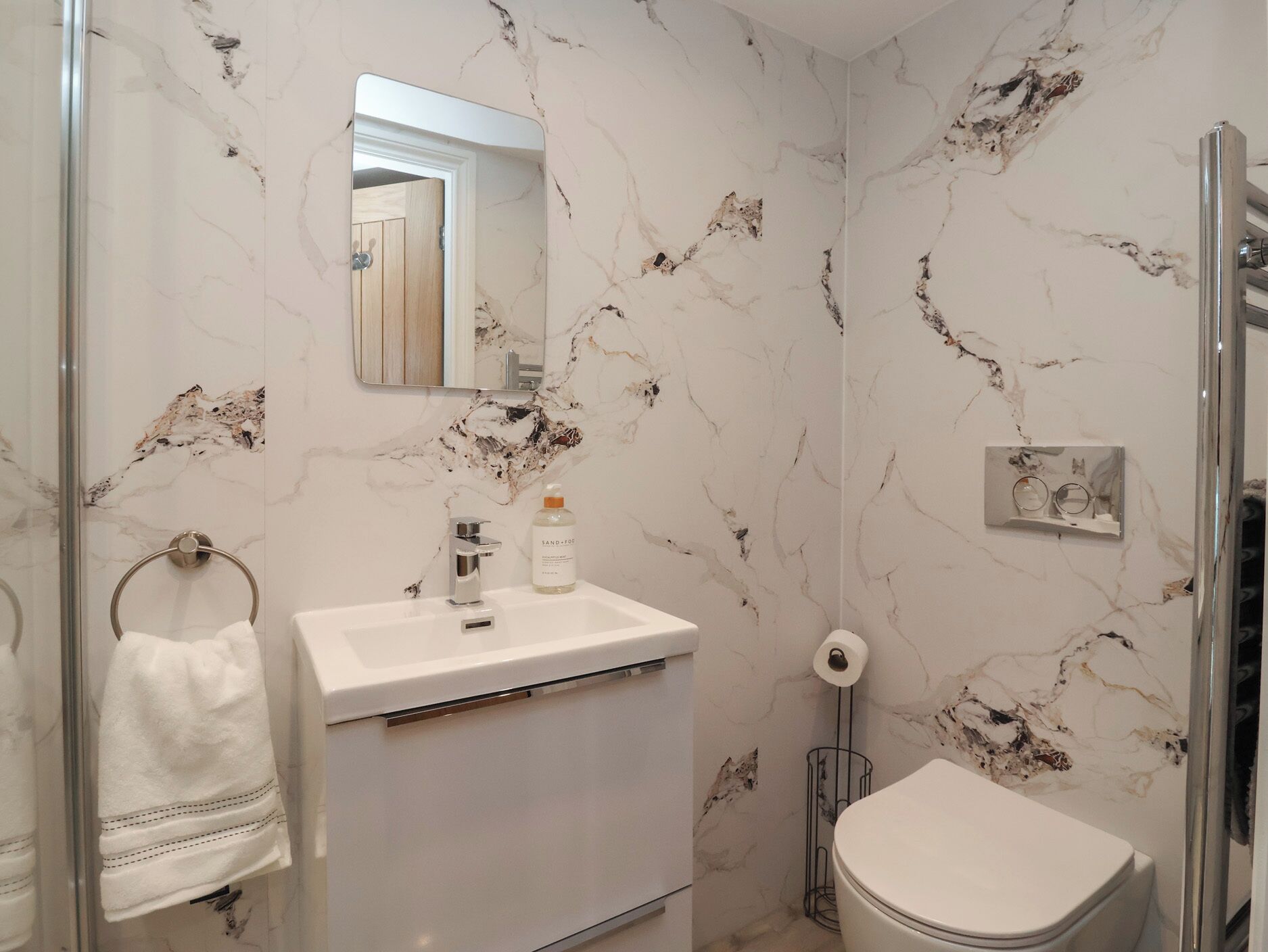 A bathroom with a marble wall, a sink, a toilet, and a towel rack.