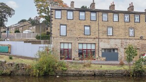 Un bâtiment en pierre de deux étages, doté de nombreuses fenêtres, d’une porte rouge et d’un petit jardin à l’avant.