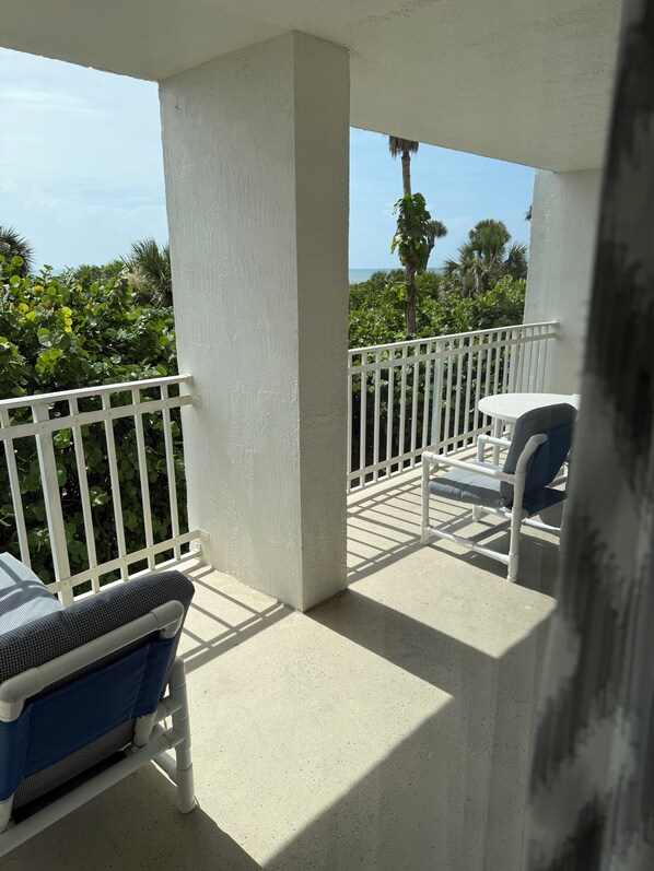 A balcony with white railings, a small table, and a chair with a blue cushion.
