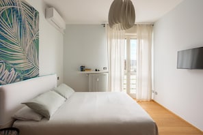 A bedroom with a bed, a radiator, a shelf with books, a television, and a window with curtains.