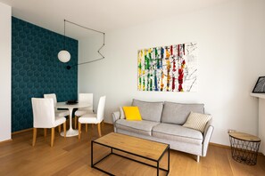A modern living room with a grey sofa, white chairs, a round coffee table, and a colorful abstract painting on the wall.