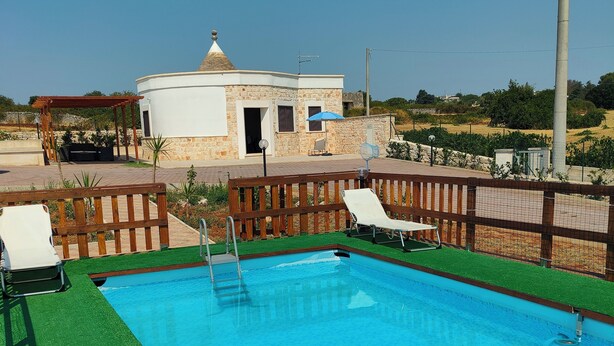 A swimming pool with a wooden deck, lounge chairs, and a stone building in the background. - Il Trullo di Antonio (Martina Franca)