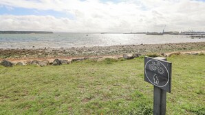 A coastal view with a grassy area and a sign indicating a bike path. - 13 Sunset Terrace Rockley Park (Poole)