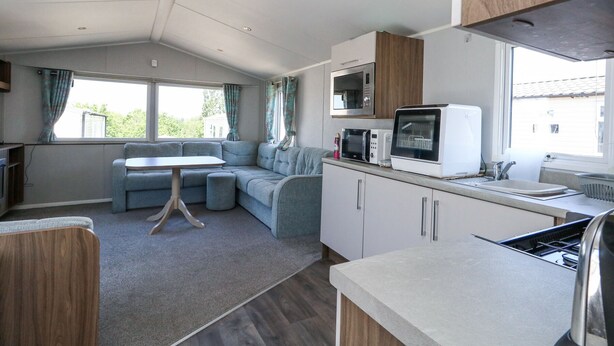 A compact kitchenette with a microwave, toaster, and sink. There is a dining area with a table and a sofa. - 13 Sunset Terrace Rockley Park (Poole)