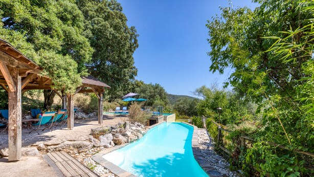 Una piscina con muelle de madera, sillas de descanso y un pabellón.