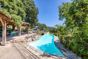 A swimming pool with a wooden deck, lounge chairs, and a gazebo.