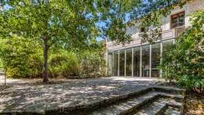 Una escalera de piedra que conduce a un edificio con amplios ventanales, rodeado de árboles y vegetación.
