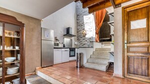 Una cocina con refrigerador, microondas y estufa, un gabinete de madera con vajilla, y una escalera que conduce a un nivel superior.