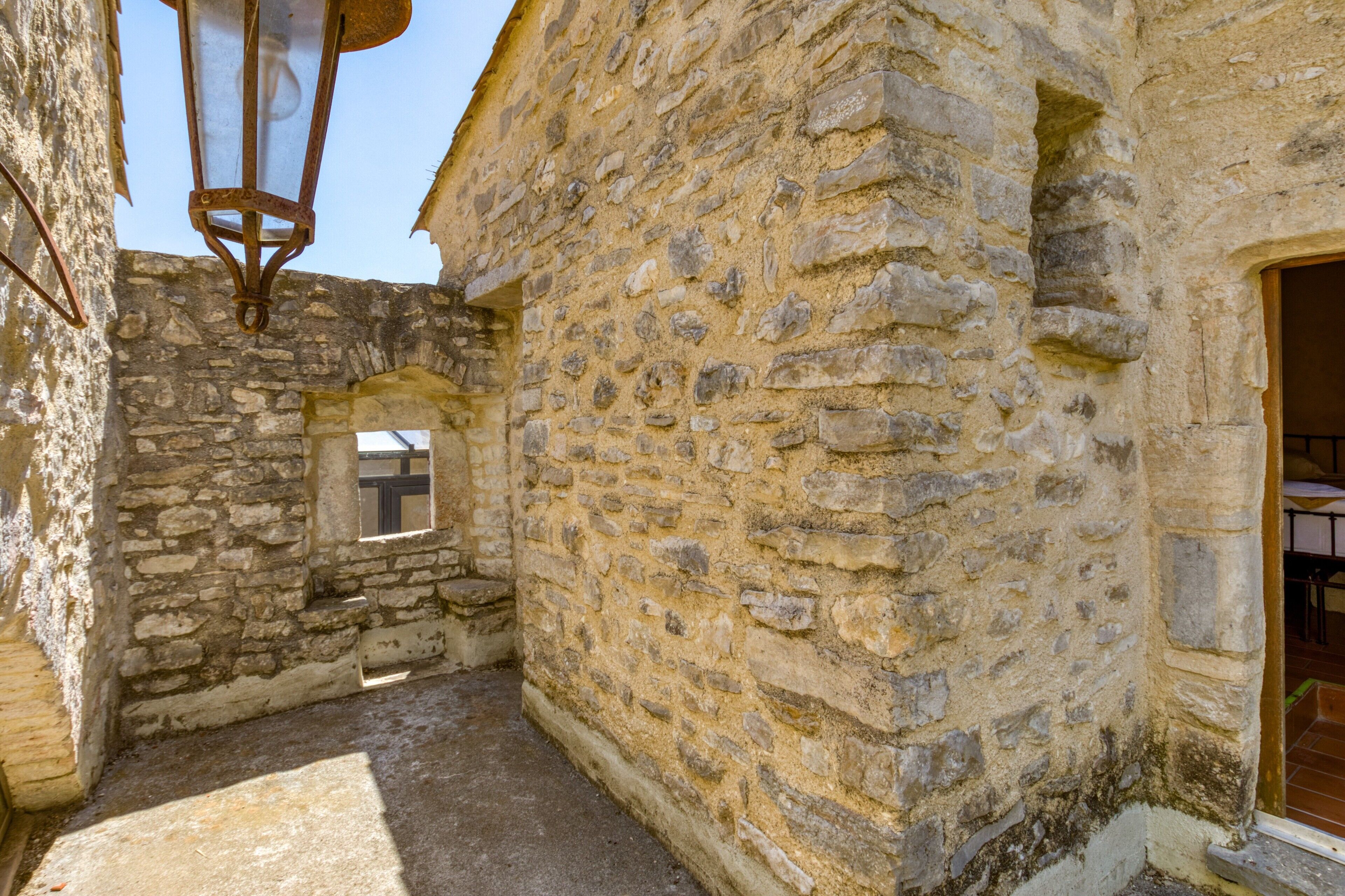 An interior courtyard with stone walls, a small window, and a hanging light fixture.