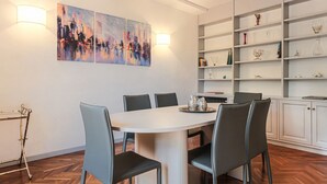 Un coin repas avec une table blanche, des chaises grises et un tableau représentant un paysage urbain accroché au mur.
