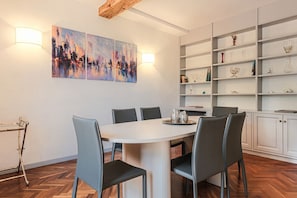 A dining area with a white table, grey chairs, and a cityscape painting on the wall.