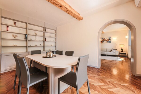 Un coin repas avec une table et des chaises blanches, un plancher en bois et une bibliothèque contenant divers objets.