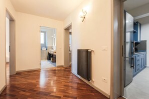 Un couloir doté d’un plancher en bois, d’un radiateur et d’un coin cuisine avec des placards et des appareils électroménagers.
