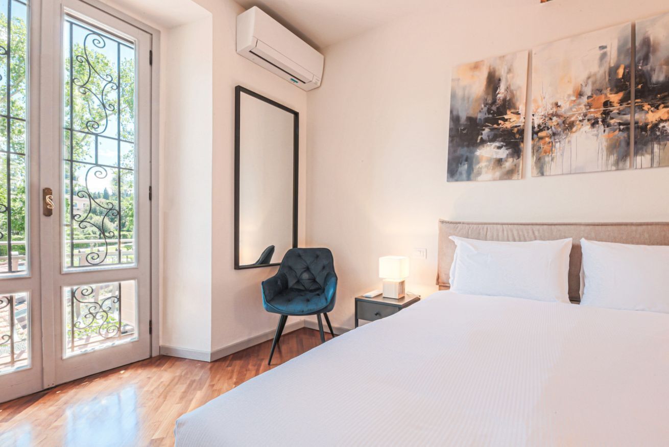 A hotel room with a bed, a chair, a nightstand, a mirror, and a painting on the wall.