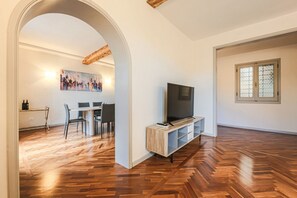 An open-plan living area with a wooden herringbone floor, a TV on a wooden stand, a dining area with chairs and a table, and a painting on the wall. - Apartments Florence - Living in Oltrarno (Firenze)