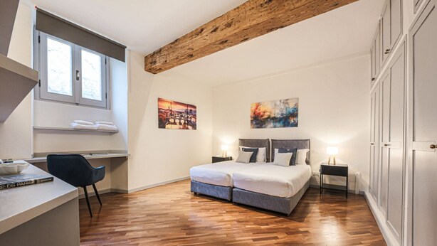 Une chambre avec un plafond en bois, un lit avec des oreillers, un bureau avec une chaise et des œuvres d’art accrochées aux murs.