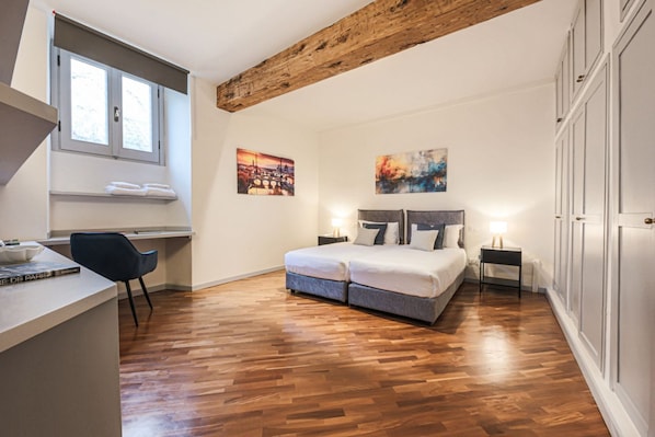 A bedroom with a wooden ceiling, a bed with pillows, a desk with a chair, and artwork on the walls.