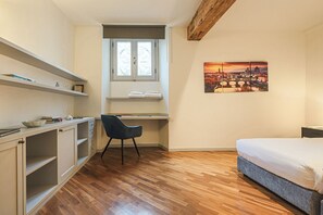 A bedroom with a bed, a desk with a chair, a window, and a cityscape painting. - Apartments Florence - Living in Oltrarno (Firenze)