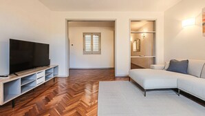 Un salon moderne avec un téléviseur à écran plat, un canapé et un parquet en bois à motifs en chevrons.